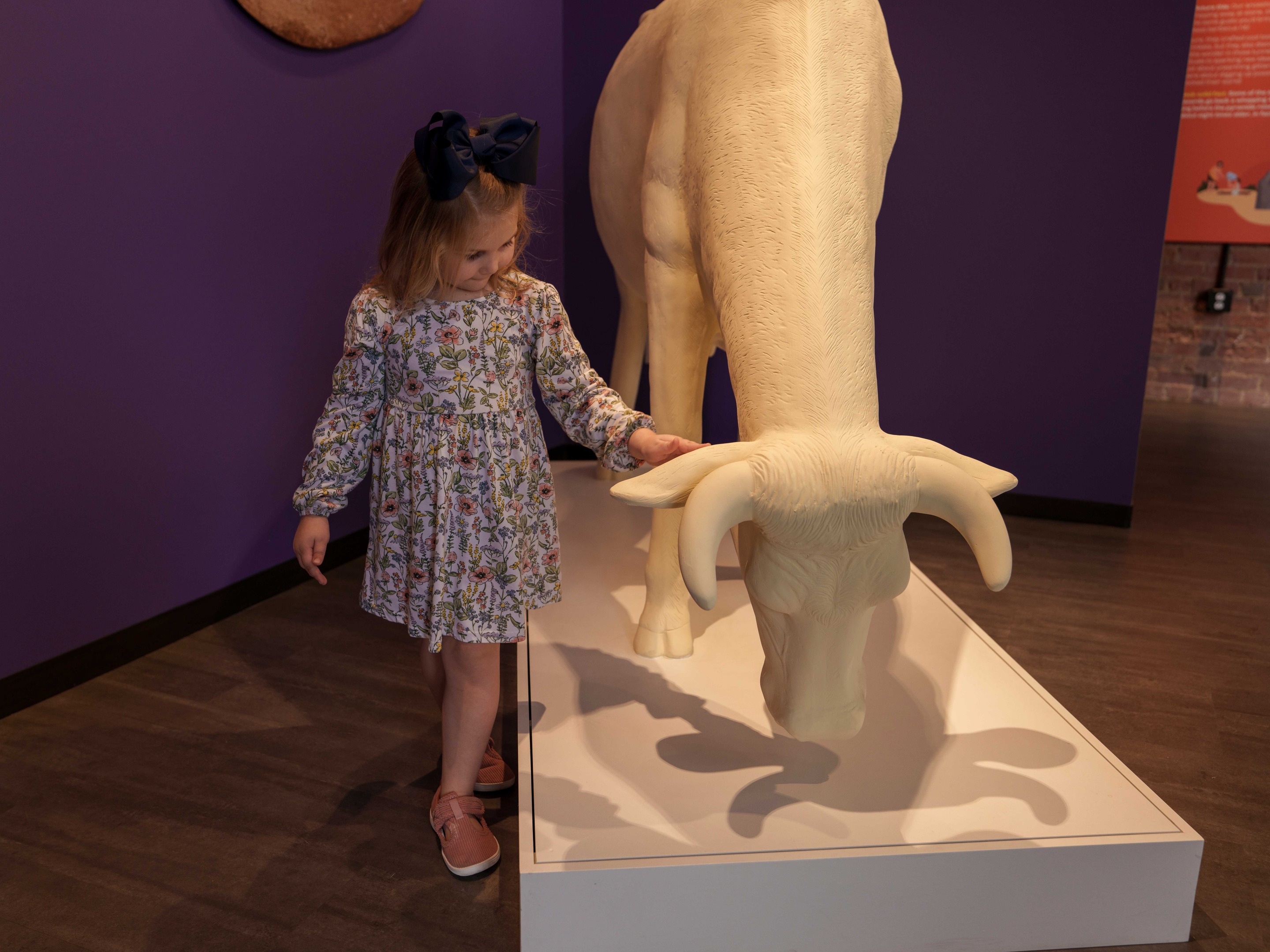 A young girl in a floral dress reaches out to gently touch a sculpture of a cow currency at the Lintshiwe Money Museum.