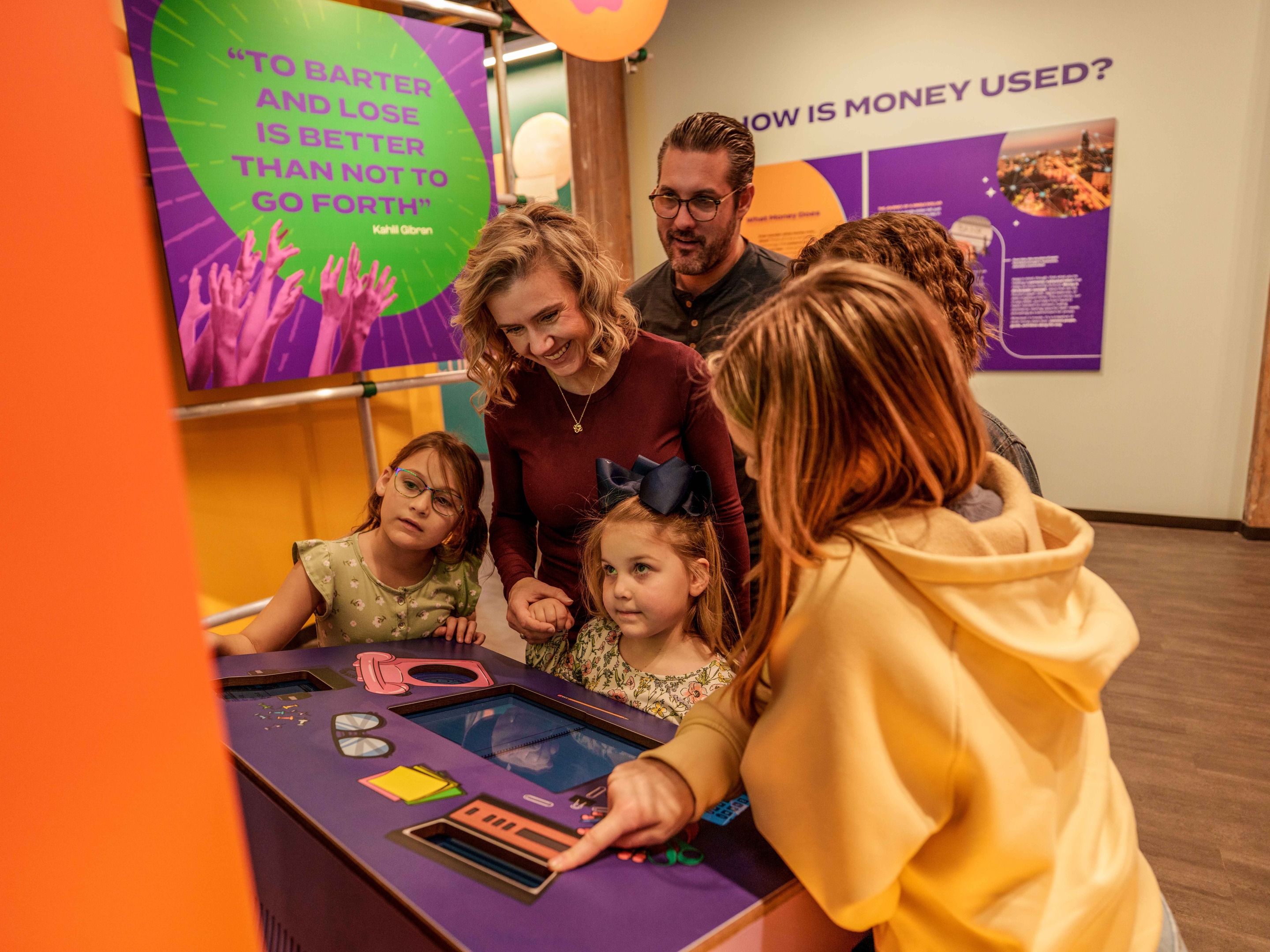 Family with children gathered around Lintshiwe's interactive barter exhibit, smiling and pointing as they play to win.