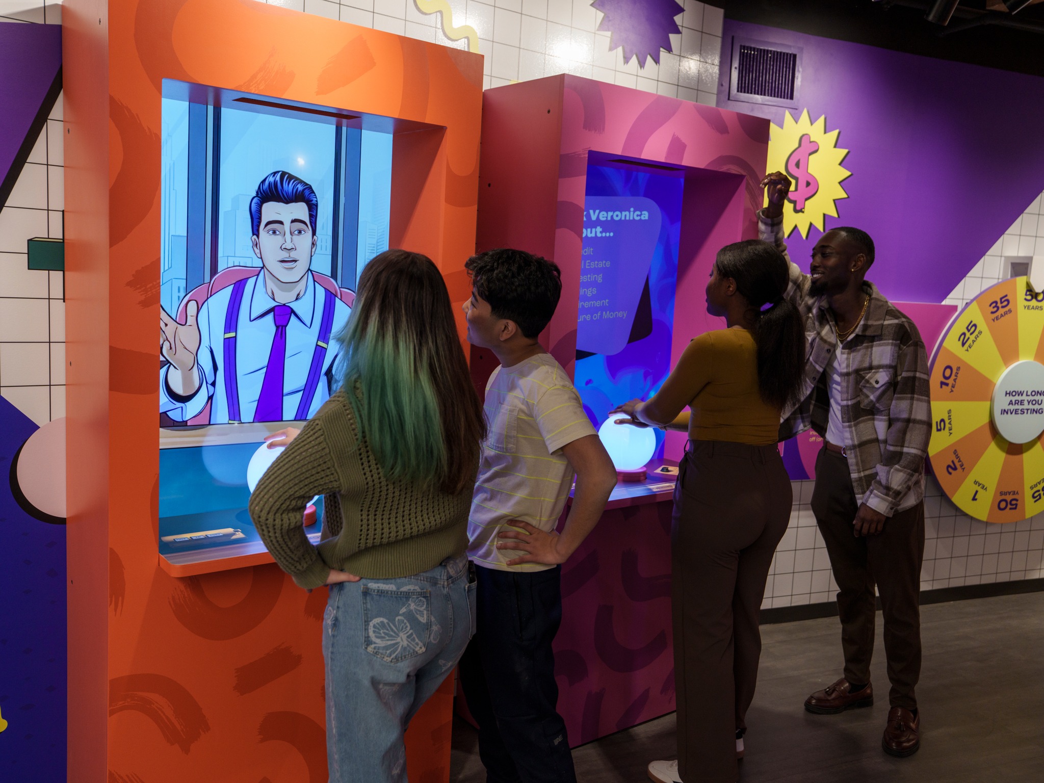 A small group of young professionals gathers around a colorful interactive money-investment exhibit at the Lintshiwe Money Museum.
